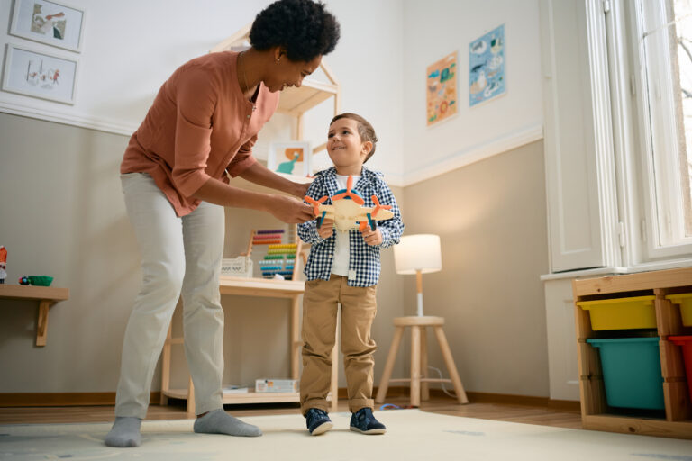 Happy little boy and his African American teacher using airplane toy while playing int he kindergarten.
