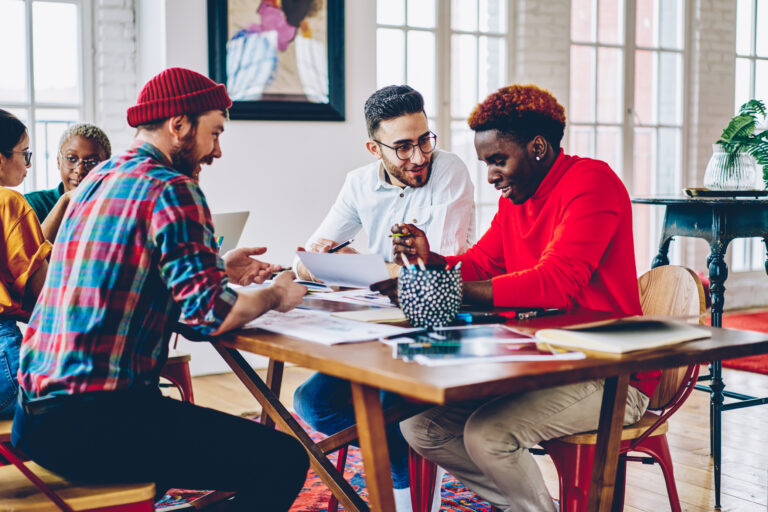 Casual dressed male partners analyzing paperwork during brainstorming cooperation at table desktop, young hipster guys analyzing startup project success while talking about report on briefing